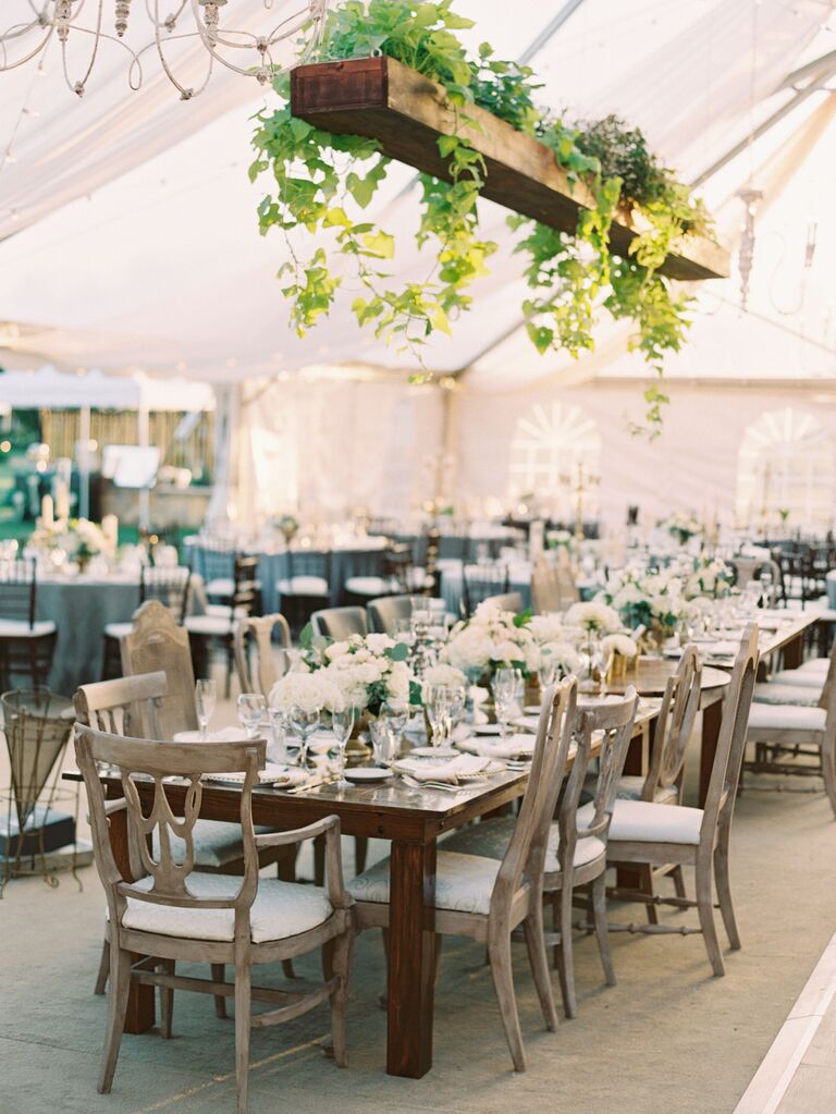 simple hanging wedding flowers with ivy vines spilling over horizontal wooden plank above dark wood table 