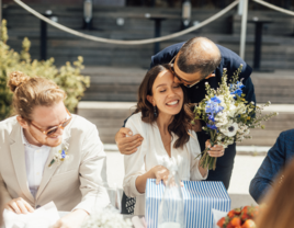 Bride receiving kiss on the head from family member while opening gifts at wedding