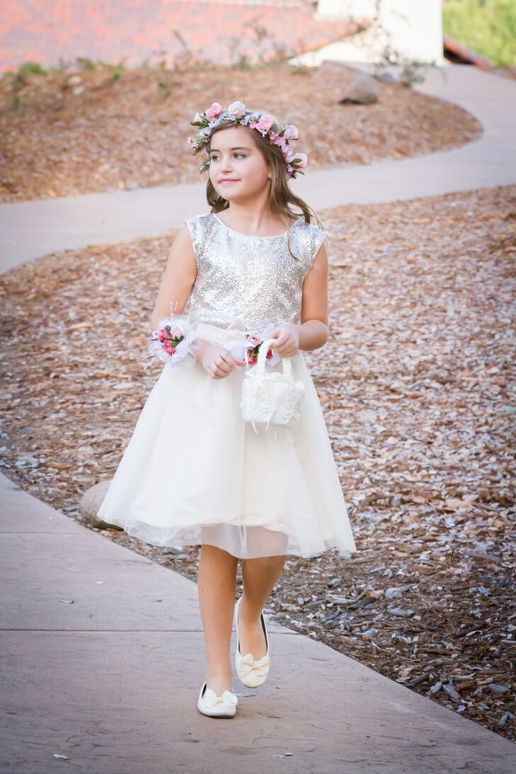 The flower girl walked down the aisle wearing a dress with a silver sparkly top that flared out into a knee-length tulle skirt. A pastel-colored flower crown was placed on top of her down hairstyle, and she held a small, white basket filled with petals.