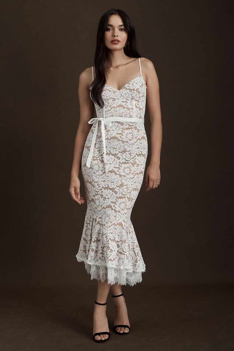Model wears a white lace gown with a belted waist. 