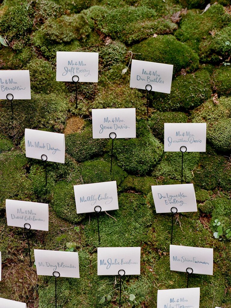 2023 wedding flower trend moss escort card wall with hand-painted escort cards on wire hooks