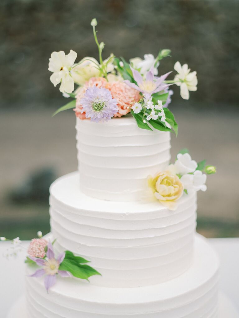 three tier white buttercream wedding cake decorated with pastel purple, yellow and coral flowers