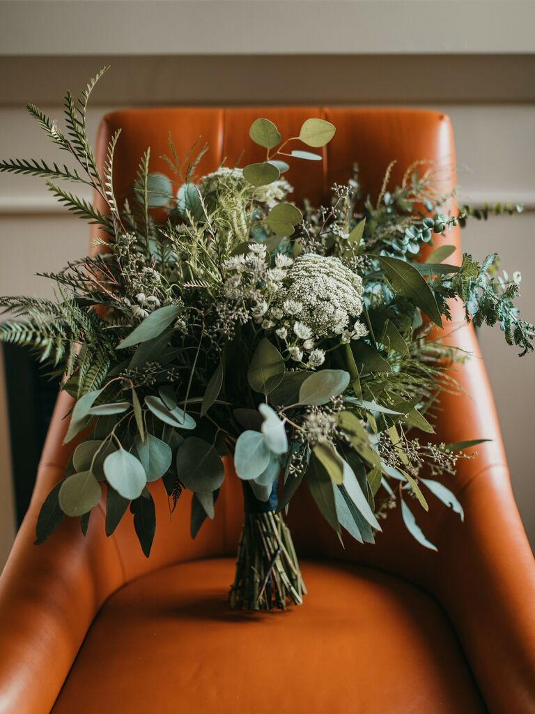 simple minimalist wedding bouquet of mixed greenery on a brown leather chair
