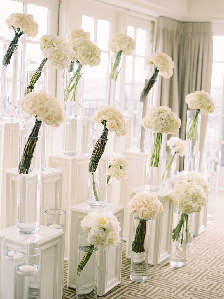 White flowers in clear vases on pillars as a flower wall idea. 
