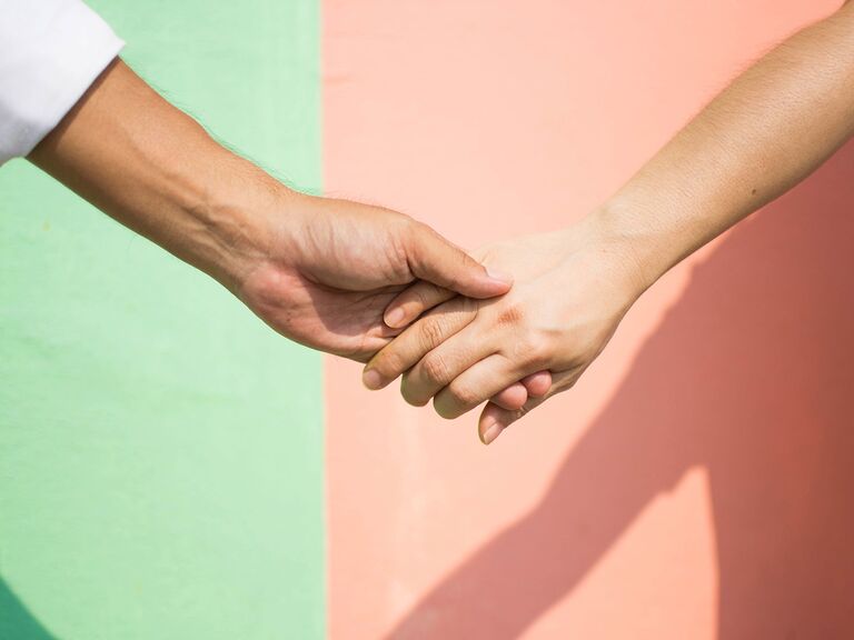 Two people hold hands against a peach and mint green background.