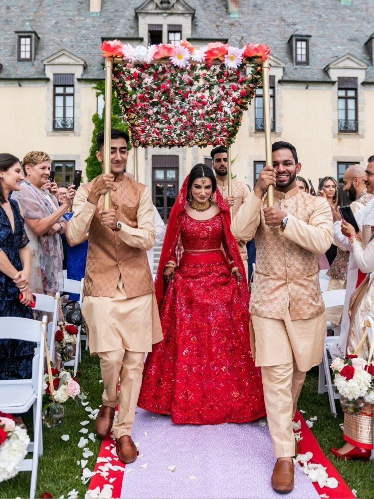 bride processing into Hindu wedding ceremony under red floral canopy
