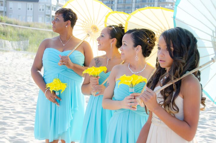 Mari's bridesmaids dressed in strapless, knee-length aqua dresses and carried yellow calla lily bouquets. They also had yellow parasols for the bright summer ceremony. Her junior bridesmaid wore the same dress in sand and carried a blue parasol that coordinated with the bridesmaid dresses.