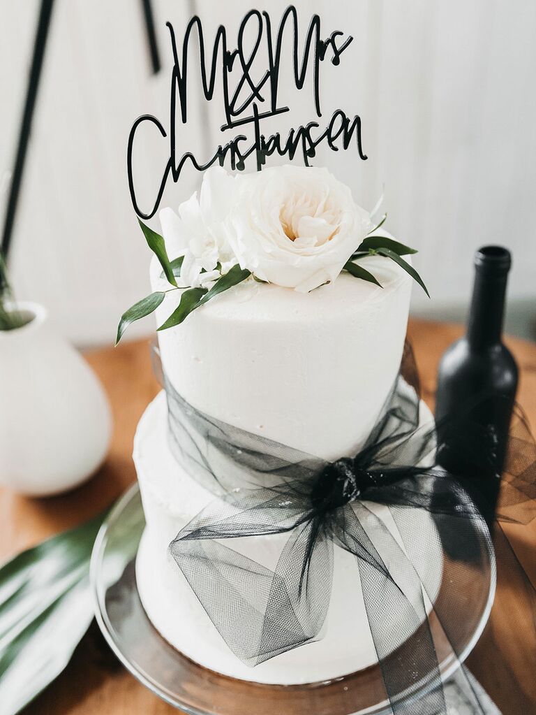 Two-tier white wedding cake with elegant black topper and black tulle bow tie