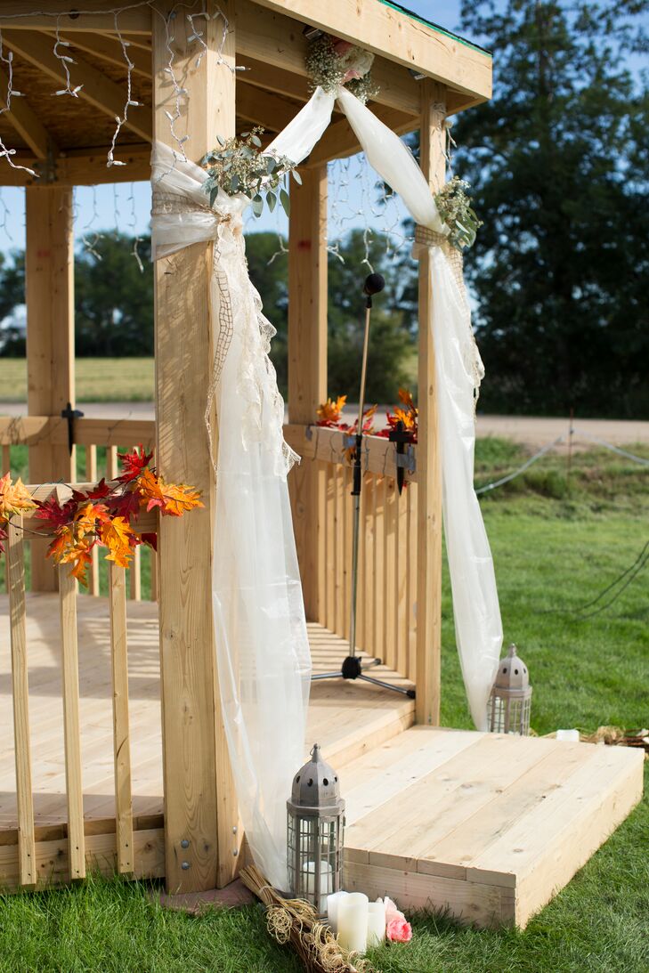 A large, wooden gazebo was built specifically for Talia and Casey's outdoor, fall wedding and was adorned with white drapery, fall leaves, candles and lanterns to complete the rustic style of the day.