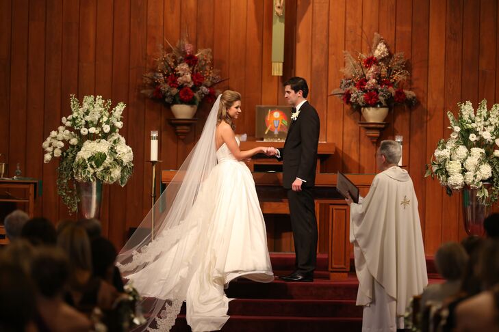 For her traditional Catholic ceremony, Kieran wore a cathedral veil with lace trim that looked beautiful with her simple ball gown. The altar at the wood-paneled church was decorated with white flower arrangements of roses, ranunculus, hydrangeas and delphiniums.