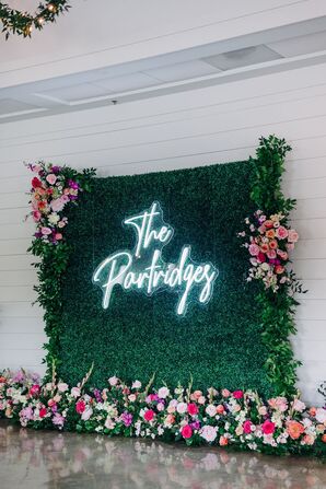 Neon Sign With the Couple's Last Name on a Floral-and-Greenery Wall