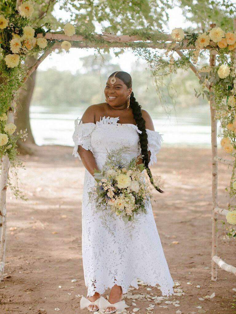 Bride holding bouquet of yellow flowers under yellow floral ceremony arch at outdoor summer wedding