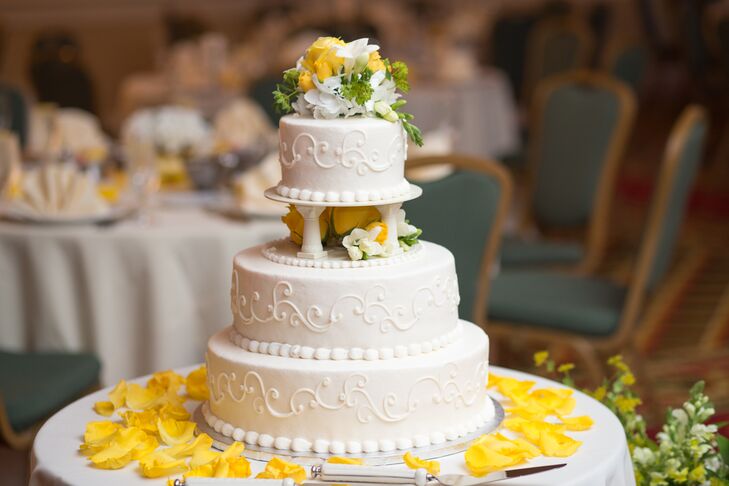 The top tier of the white wedding cake was elevated by little pillars. The cake was decorated with piping, yellow roses and white freesias. The cake table was also scattered with yellow rose petals. The cake was flavored butter rum with raspberry ganache—yum!