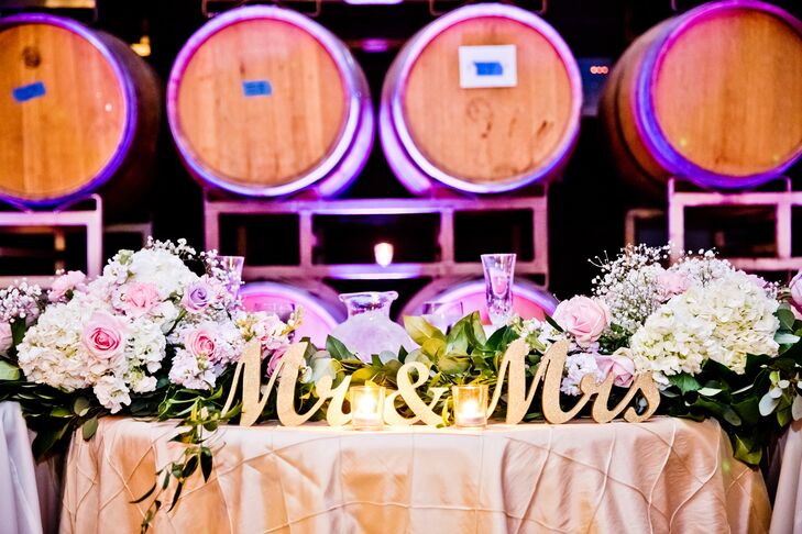 Joanne and Rainnier took their seats at the sweetheart table, which was labeled with a gold sign that read "Mr. & Mrs." The top of the table was decorated in overflowing lush pastel roses, hydrangeas and baby's breath arrangements.