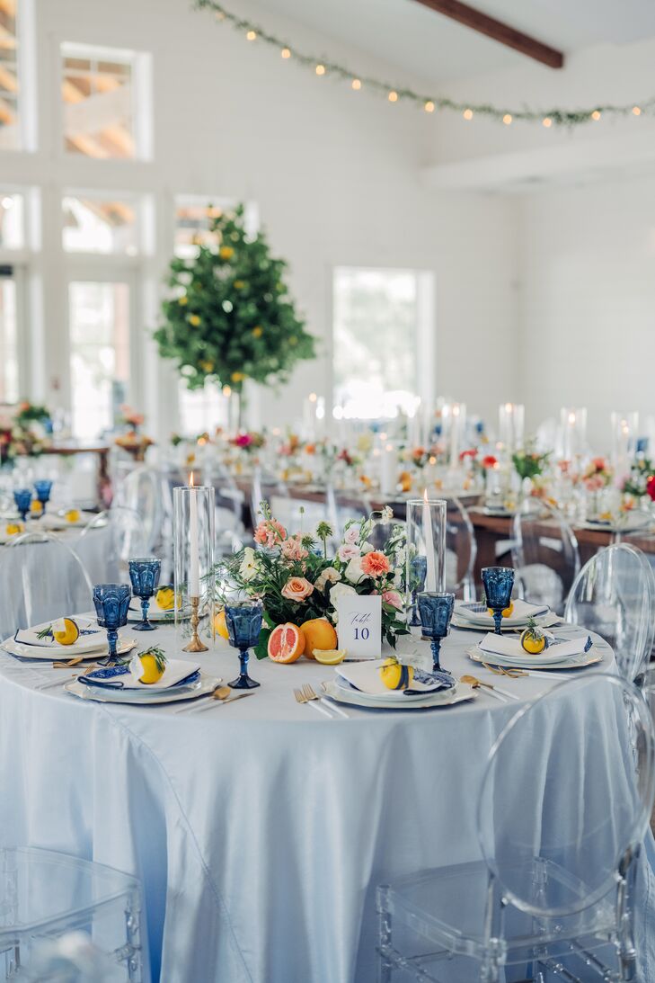 Round reception tables with blue table linens, blue water goblets, low centerpieces with blush-colored flowers and citrus at an Amalfi-Coast-inspired wedding reception.