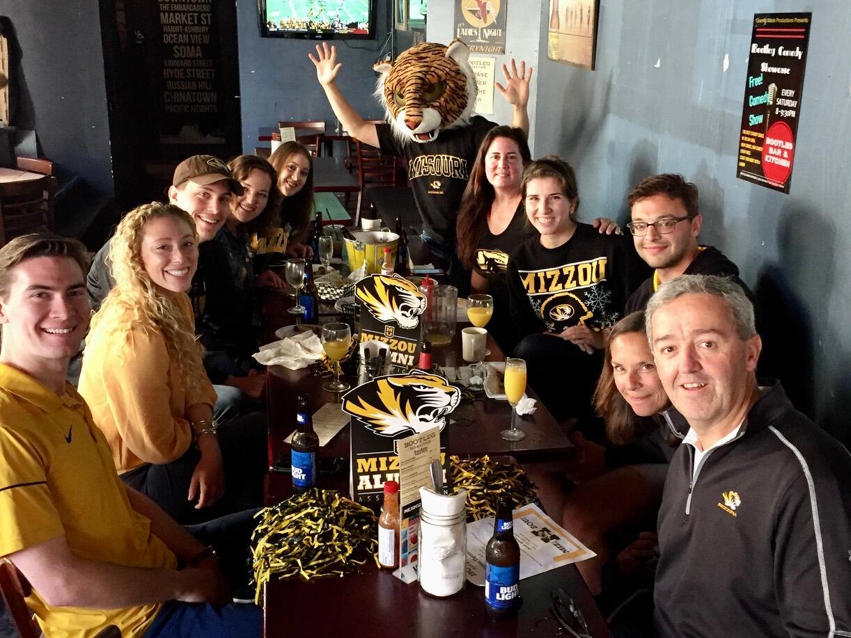 It was a brisk San Francisco morning and Mizzou was playing Georgia at 9 a.m. PT, a questionable time for football. Joe’s parents, Jane and Charlie, were visiting and didn’t want to miss the SEC showdown. Joe had heard of a Mizzou alumni bar in town and figured they could stop by to watch the game and say a quick hello to fellow Tigers. Little did he know, Veronica was the president of the local Mizzou alumni chapter and had a deal with the bar to only open for Mizzou fans before noon.

Joe and his parents stepped into the nearly empty bar and discovered a table of eight people inhaling fried pickles and mozzarella sticks for breakfast. “Did you guys rent this entire bar out?” Joe asked, perplexed. “Pretty much, yeah,” Veronica replied. Decked out in Mizzou gear, the newcomers were quickly welcomed into the group and provided with the finest Budweiser bottles (aka Charlie’s drink of choice, so practically champagne). Jane and Charlie even knew someone on Mizzou’s coaching staff at the time, so naturally, a group photo was taken within minutes of meeting.

After Georgia reminded Mizzou who’s boss, Veronica’s friends decided the day was still young. Their next stop? A bar called The Lot, which was literally a parking lot that served rosé and beer on uncomfortable benches. Knowing this sounded less than appealing, but wanting the newcomers to stick around, Veronica pitched it to them with all the charm she could muster: “It’s a really cool spot, they have benches and port-a-potties.” Sales was never her calling, but somehow, it worked and off they went.