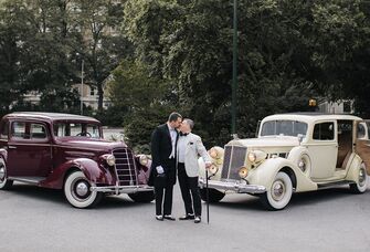 two grooms kissing in front of two classic cars