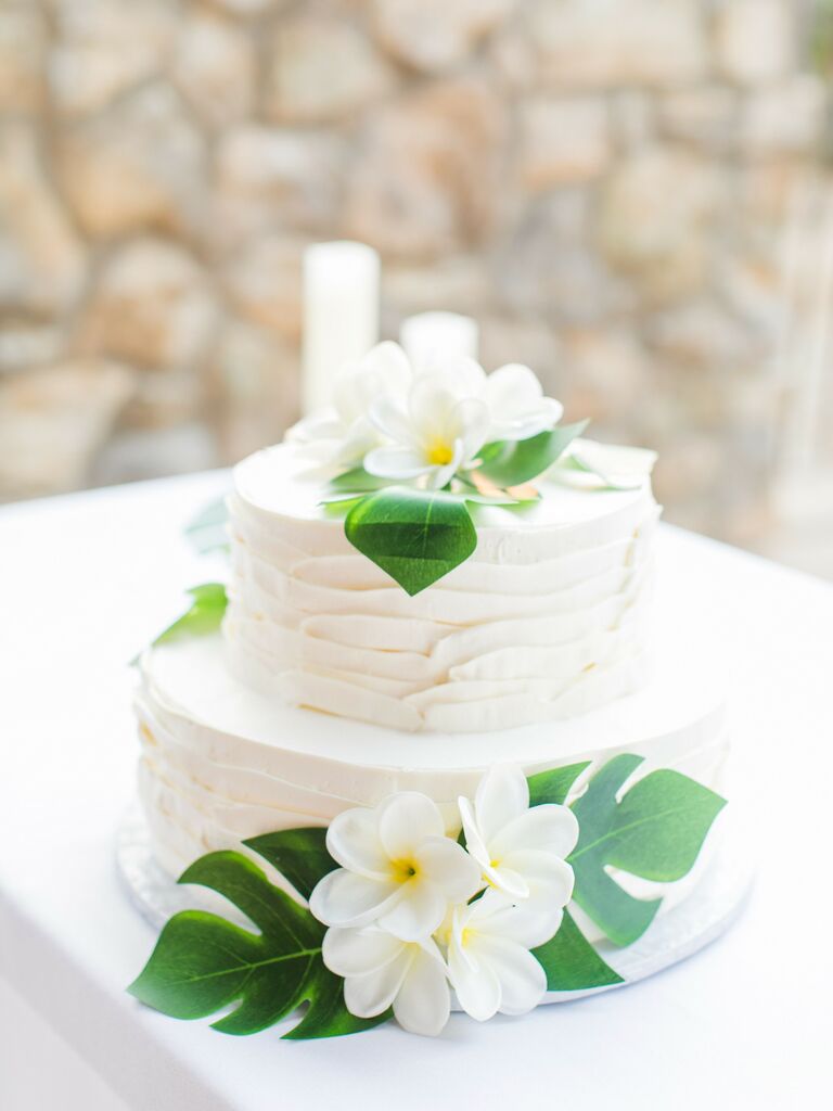 two tier buttercream wedding cake with monstera leaves and white plumeria flowers