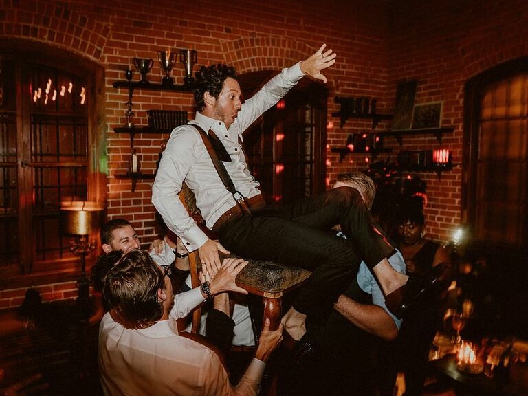 Groom being lifted on a chair at a wedding after-party. 