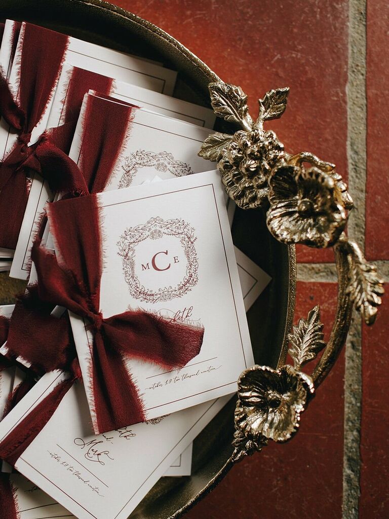 wedding ceremony programs with custom crest and dark burgundy silk ribbons displayed in a bronze tray