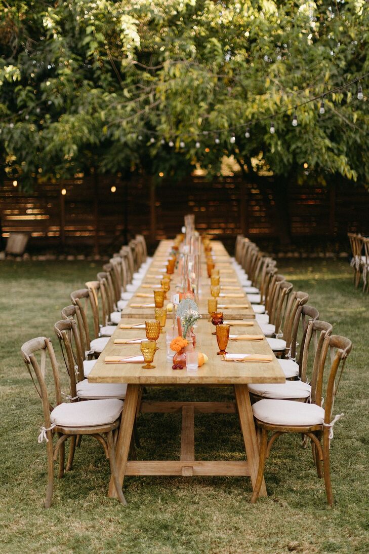 Long, Wooden Table With Minimal Decor, Burnt Orange Glassware Under String Lights