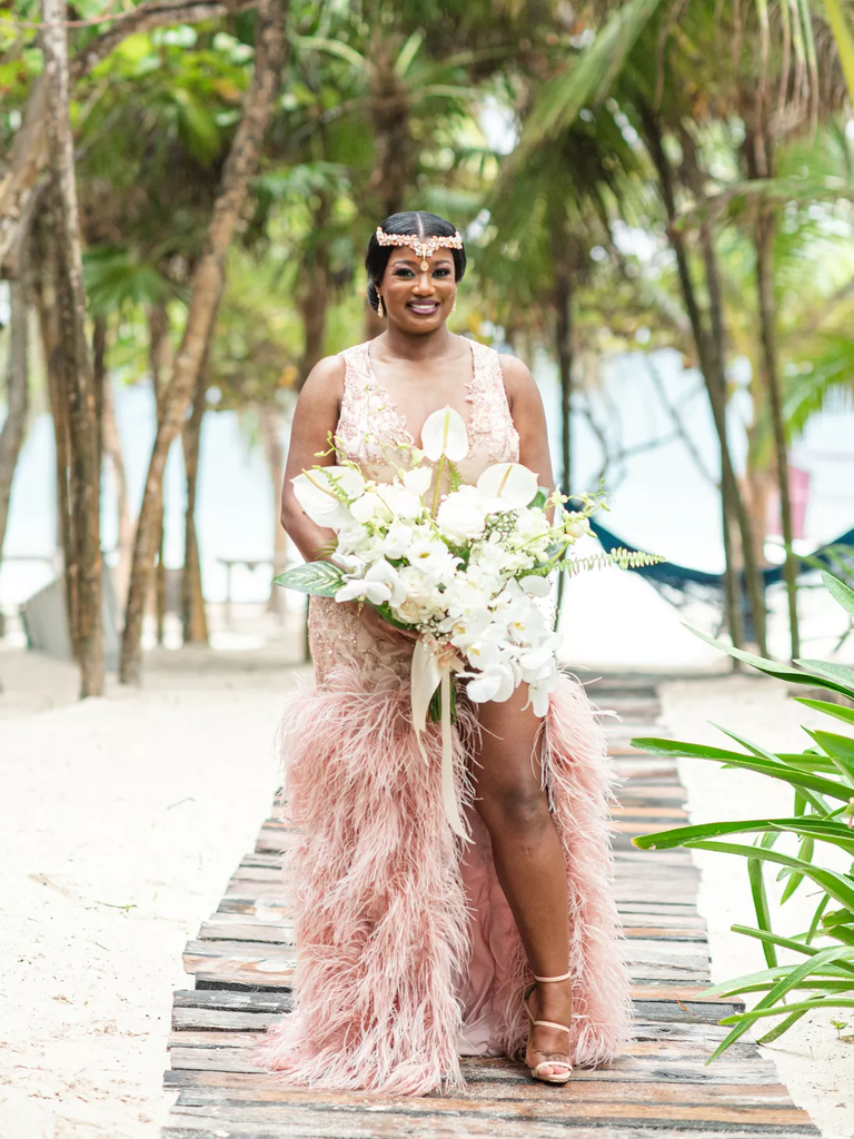 A bride walks down a beach pathway in a stunning modern dusty rose wedding dress.