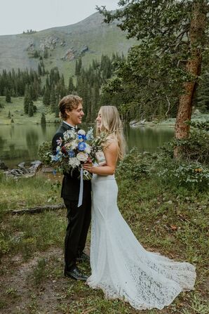 Bride in Lace Gown and Groom in Suit Hold Colorful Bouquet of Wildflowers at Lakeside Venue