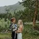 Bride in Lace Gown and Groom in Suit Hold Colorful Bouquet of Wildflowers at Lakeside Venue