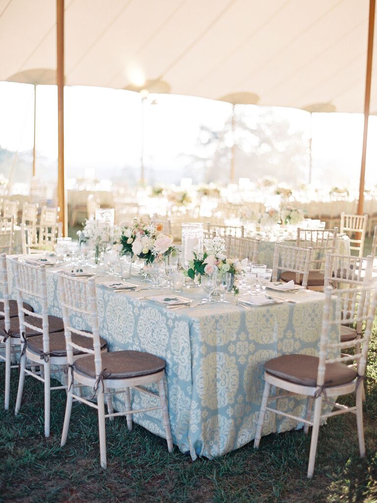 tented wedding reception featuring rectangular table decorated with pastel blue patterned tablecloth and white chiavari chairs