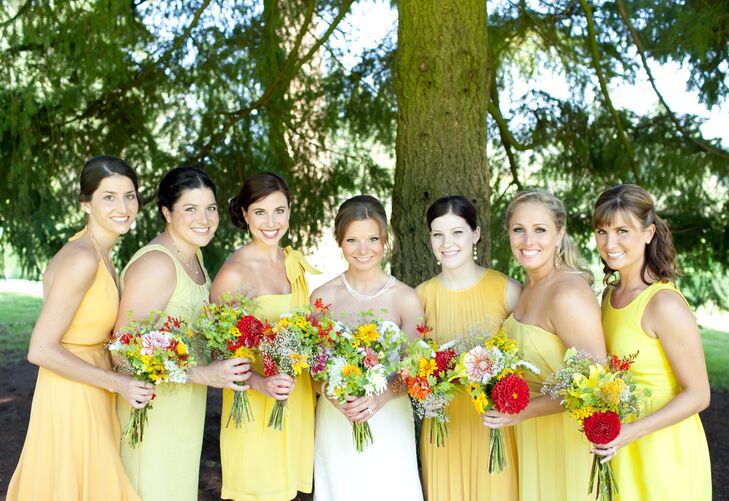The bride stood with her bridesmaids dressed in a variety of yellow dresses, each holding a colorful bouquet of flowers.