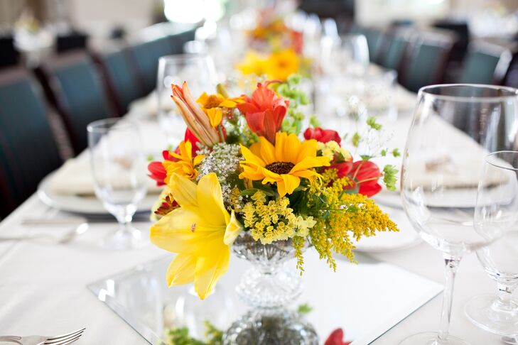 Yellow and red flower centerpieces decorated reception dining tables, filled with summer pickings of sunflowers, lilies and stock.