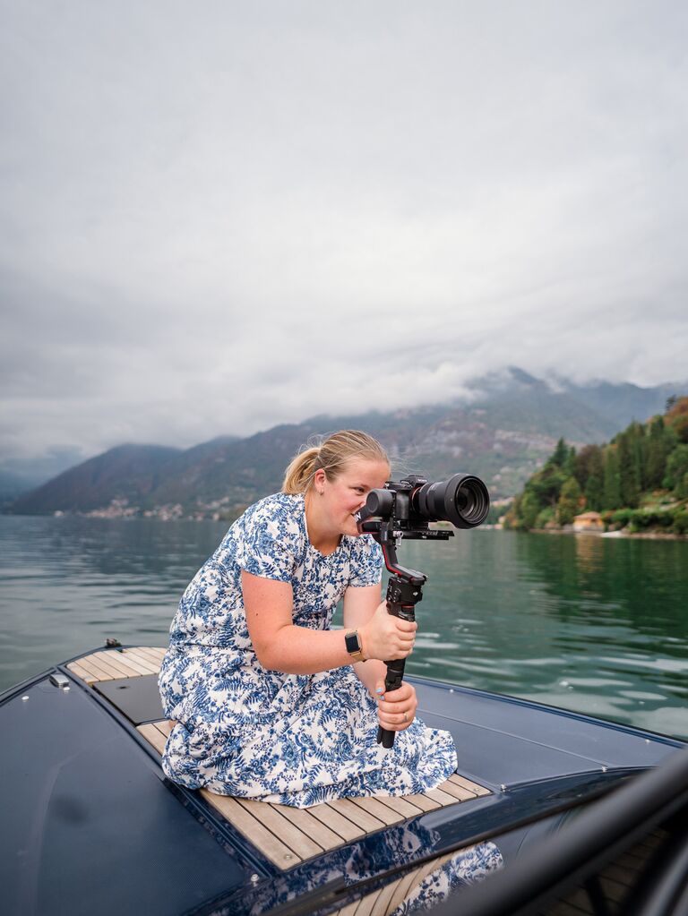 A videographer sits on the bow of a boat so she can capture the best shot.