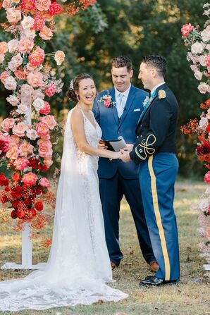 Bride Smiles at Ceremony Guests Holding Hands With Military Groom Under Bright Flowers
