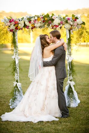 First Kiss Under Yellow and Pink Floral Wedding Arch