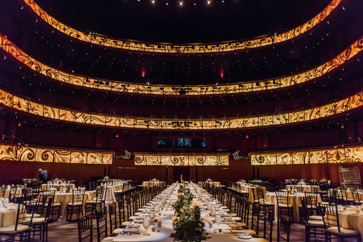 To go with the dramatic performance hall, Millie and Luke had a center head with 50 guests, surrounded by smaller round tables. The tables were covered with light pink cloths,  runners of seeded eucalyptus and elegant gold accents. Every seat included a menu what was at the dinner stations.
