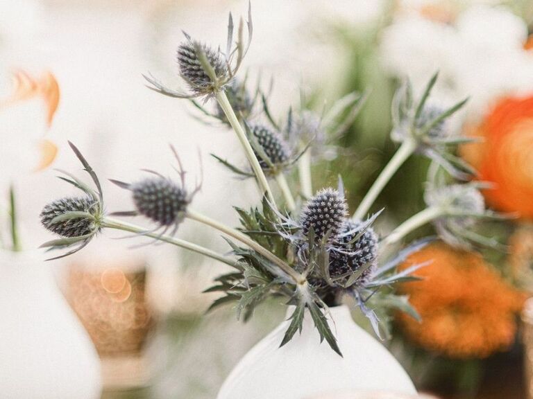 A white bud vase with blue thistles 