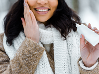 woman in winter attire putting on moisturizer
