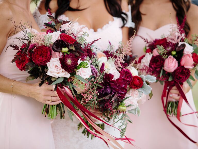 Bridesmaids hold vibrant wine-toned and pink bouquets.