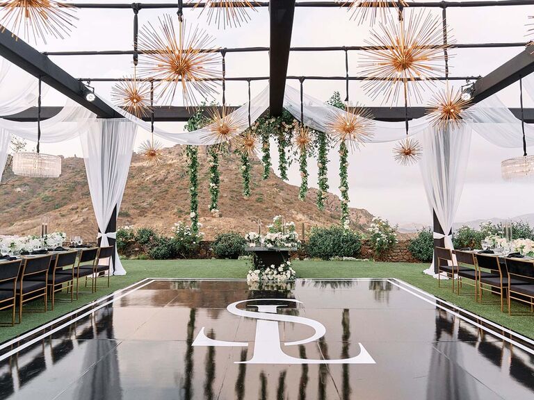 modern outdoor wedding reception with black dance floor and gold hanging light fixtures