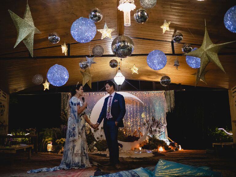 Bride and groom making speech under hanging star accents and illuminated disco balls at celestial wedding