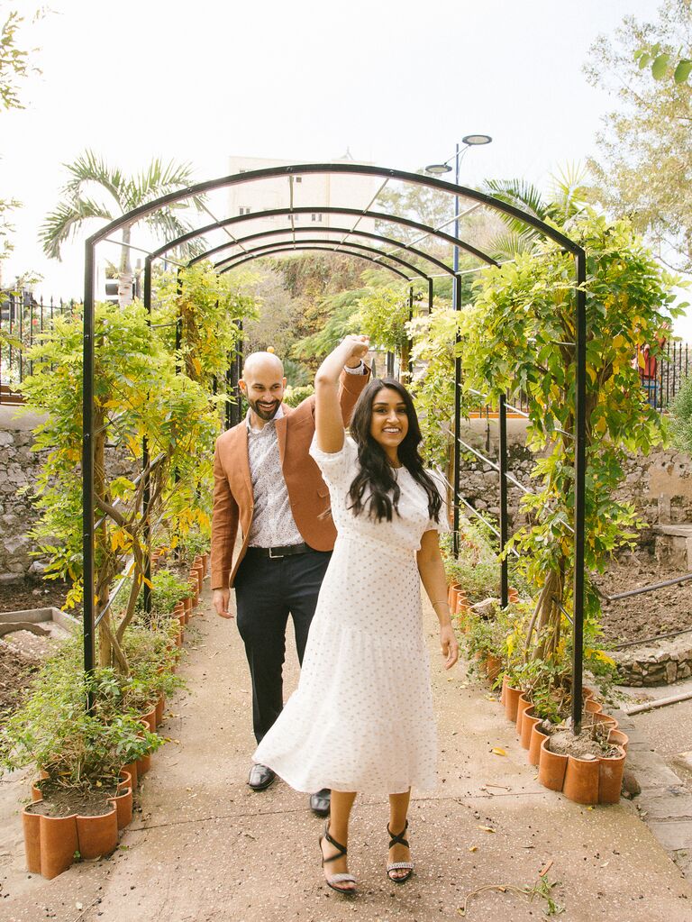 A man and woman twirl under a greenery-laden archway for their engagement photo session