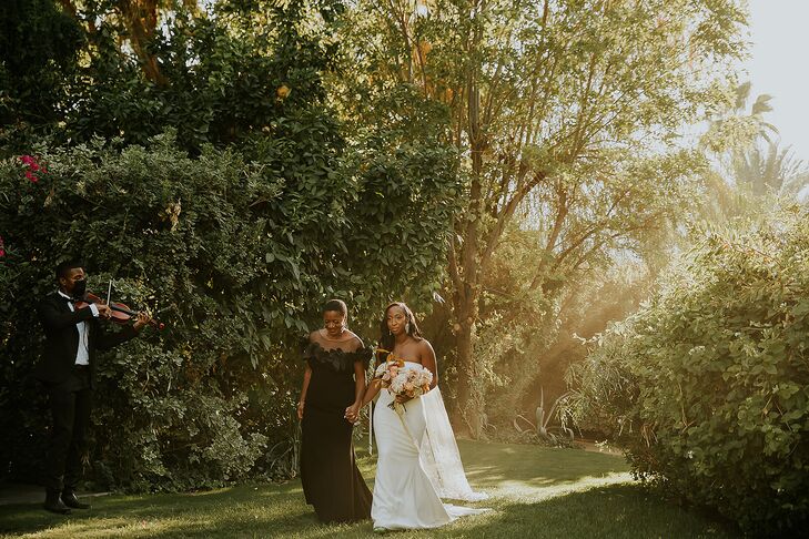 Bride's Mother in Chic Black Dress Leads Bride in Modern, Sleek Gown Down Garden Aisle Through Trees