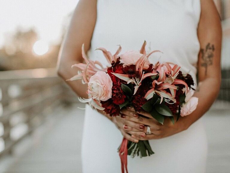 Bride holding autumnal bouquet with red and pink flowers at fall wedding