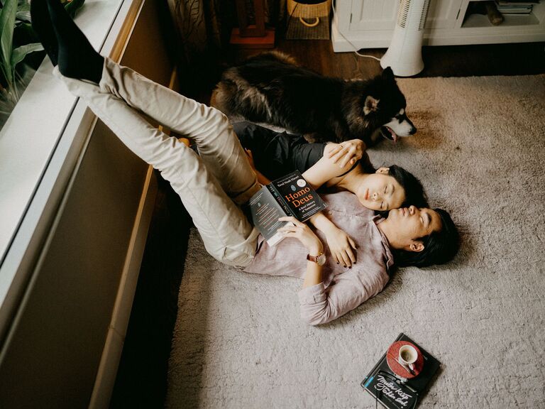 Couple cuddles on the floor with their dog next to them. 