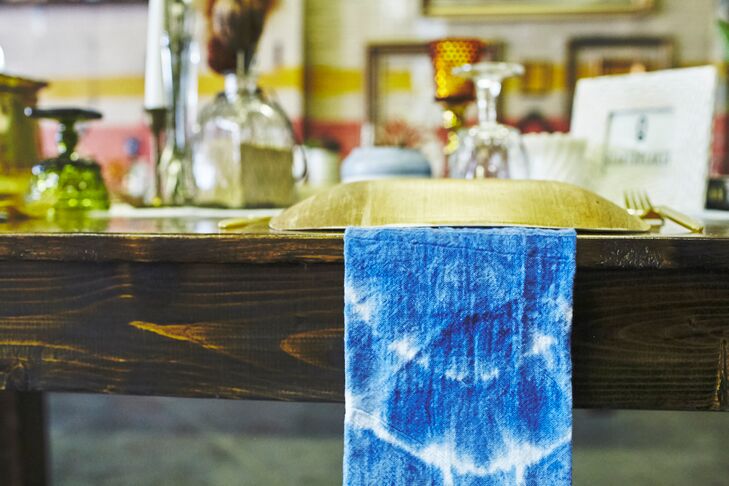 Family members helped the couple dye Shibori napkins for each place setting. Square plates that were made out of biodegradable plant leaves were paired with gold plastic silverware.