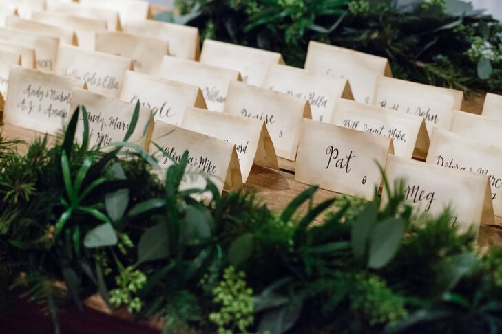 For the escort cards, Lily turned to her friend and bridesmaid from Merely Mere. She designed the stationery and gave it that vintage feel by hand-dipping each one with tea bags. Then she used her practiced skill in calligraphy to give them an added elegant flair. Lush greenery surrounded each row to tie in their forest-like theme.