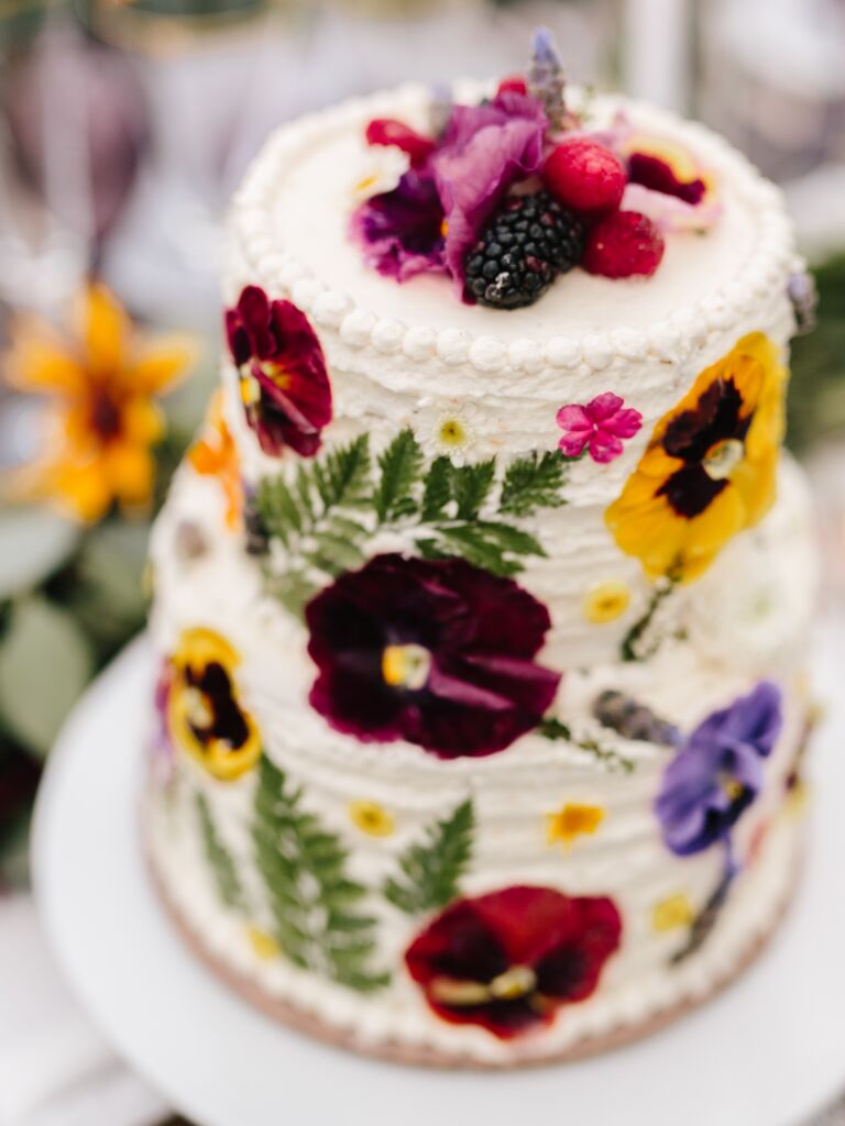 two tier buttercream wedding cake decorated with pressed pansies and fresh berries