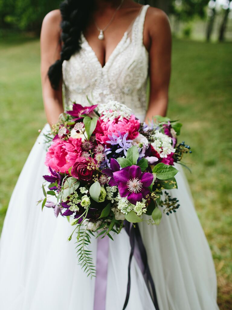 bride holding bouquet of magenta peonies and purple flowers with greenery