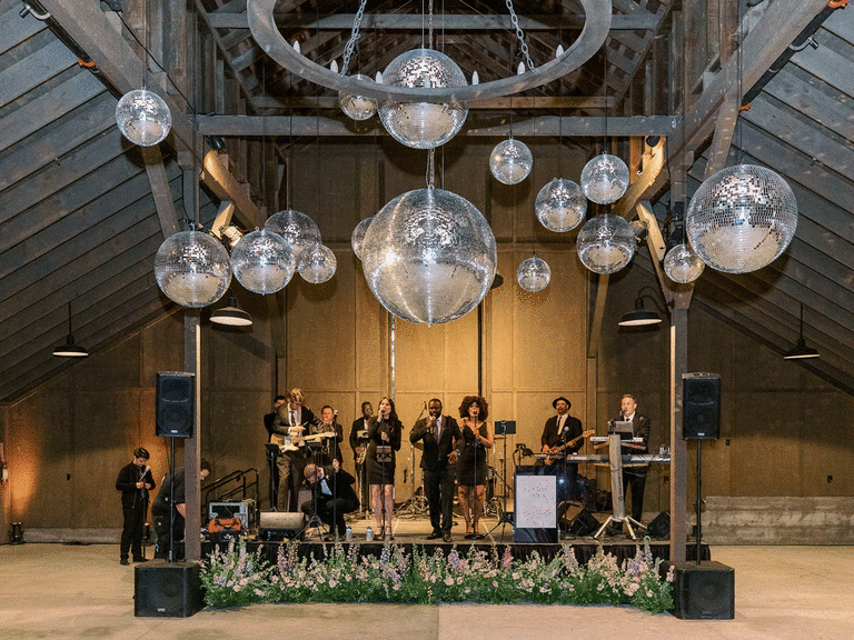 Wedding band performing in a barn with multiple disco balls above them. 
