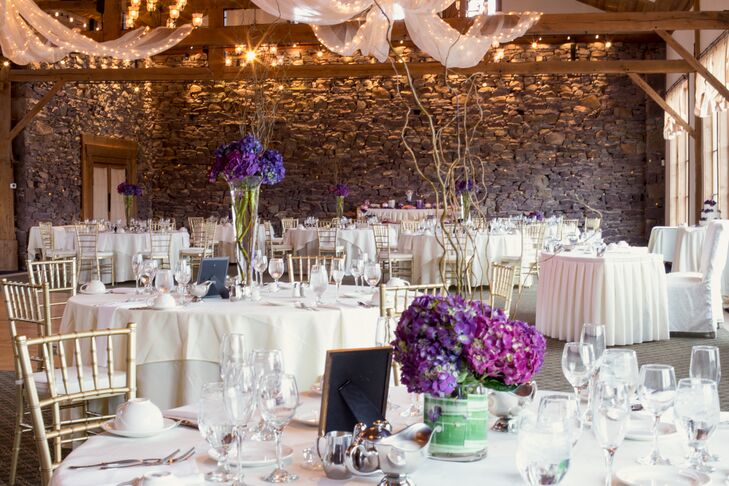 “The flowers were unique,” Sarah says. The couple’s florist, Chantilly Floral Boutique, accented their all-white decor with fun arrangements of purple hydrangeas, pink hydrangeas and branches. Each low or tall centerpiece was paired with a simpler gold and purple table number with a dotted design.